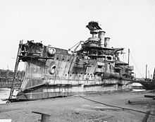 A stern view of an incomplete ship sitting in a drydock with the top of the main turret open, awaiting armor plates.