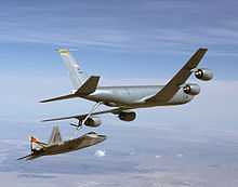 Rear/starboard view of aerial refueling tanker transferring fuel to a jet fighter via a long boom. The two aircraft are slightly banking left.