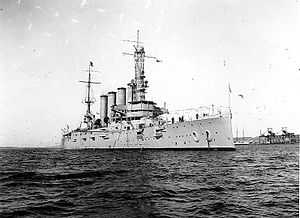 An armored cruiser anchored, with a navy jack flying from the jackstaff.