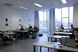 A spacious classroom with teenage students working in pairs at desks with laptop computers.