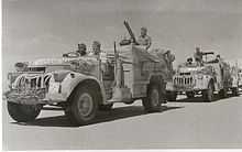 vehicles in convoy, each crewed by three men, in a desert terrain