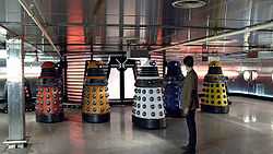 The Eleventh Doctor standing before five Daleks in a bright metallic room