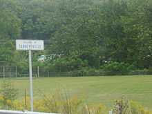 Blue and white sign denonating "Village of Tannersville" with a green field and local development in the background