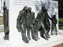 Bronze sculptures of seven figures marching stand around a large rectangular block of white engraved granite.