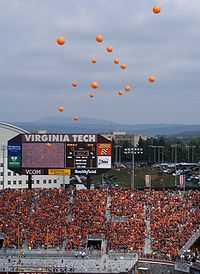 Orange balloons rising above Lane Stadium, with everyone in the stands wearing maroon or orange, and the stadium scoreboard in the background.