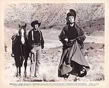 Printer poster with a photograph and text underneath. A man is standing holding the reins of his horse. A woman is running towards the camera. They are in a dry landscape with a stony canyon wall in the background. The text consists of a copyright notice and a license for periodicals to reproduce the photograph.