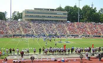 Football stadium with two teams on the field and stands full on sunny day