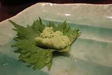 Dab of wasabi on a green shiso leaf, possibly at a sushi-bar counter