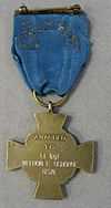 Back of a bronze cross-shaped medal hanging from a blue ribbon