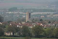 Multiple houses with prominent square tower. Hills in the background.