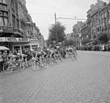 A group of cyclists passing through a city, watched by many spectators