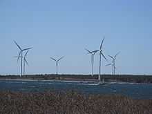 Seven three-blade wind turbines on the shore. A fishing boat is passing by. 