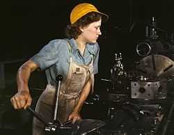 Woman in a yellow cap turning a wheel in a factory