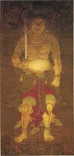 Frontal portrait of a frightening deity dressed only in a skirt-like garment holding a sword in his right hand.