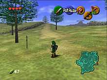 The child version of the game's protagonist, Link, stands in Hyrule field wearing his distinctive green tunic and pointed cap. In each corner of the screen are icons that display information to the player. In the upper left-hand corner there are hearts which represent Link's health, in the lower left-hand corner is a counter which displays the quantity of Rupees (the in-game currency) possessed by the player. There is a mini-map in the lower right-hand corner, and five icons in the upper right-hand corner, one green, one red, and three yellow, which represent the actions available to the player on the corresponding buttons of the N64 controller.