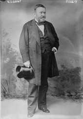 Grant is standing in a civilian dress suit holding a top hat.