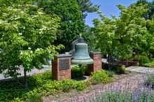 A brass bell displayed beside a sidewalk and trees