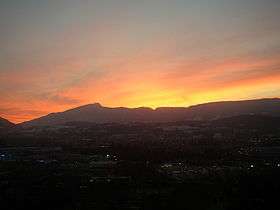 Sunset lights up the sky, silhouetting a long, notched ridge with a prominent peak toward its left-hand (southern) end.