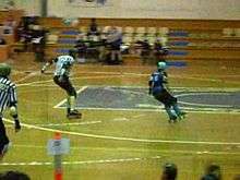 A roller skater circles the track while a referee points at her