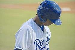 A man in a blue baseball uniform with a navy hat enters the baseball field