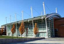 Ground-level view of a building with white poles sticking up from its sides and with trees in autumn colors in front of it