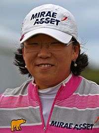 A brunette in a white hat with black lettering and gray and pink striped shirt