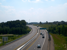 A four lane freeway dives into a ravine and back out, surrounded by rural land on both sides