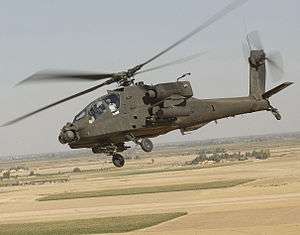 Photo of tilted horizon showing helicopter flying above barren land with rectangular patches of green grass.