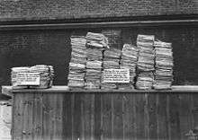 Black and white photograph of two stacks of documents on a table. The stack on the right is much larger than that on the left.