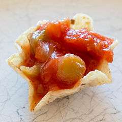 A close-up view of a tortilla chip filled with salsa