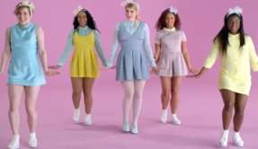 Five women dancing in an uncharacteristic wardrobe afront pastel-colored pink backdrop.