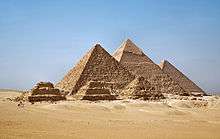 The three main Pyramids at Gizeh shown rising from the desert sands with three smaller pyramids in front of them