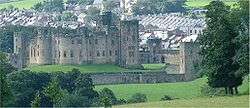 A large castle, with a ditch and trees in front of it.