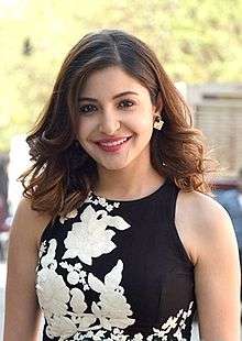 Anushka Sharma in a black sleeveless top smiling directly at the camera.