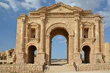 Looking North, a large stone arch can be seen, bathed by the light of the sun on the golden stone. It has many decorative features, and a smaller arch on each side of the central one.