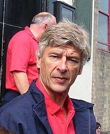 A head-and-shoulders photograph of a gentleman in his 50s. He is wearing a red polo shirt underneath a blue coat, he has grey hair, and his eyes are slightly closed.