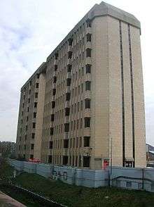 A nine-storey concrete office building sits behind a blue-painted retaining wall beside a railway cutting.