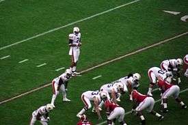 A quarterback is behind the offensive line preparing to take a snap.