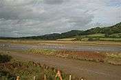 Three wooded hills loom high above a muddy estuary