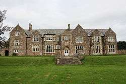 stone building with slate roof, with windows on central two bays, partly obscured by trees