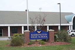 A blue sign with gold lettering reading "BARRINGTON HIGH SCHOOL" stands in front of the school.