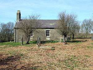 A simple stone church seen from the south. The only visible features are a west bellcote and two windows