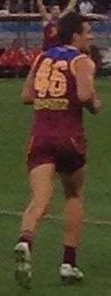 A man wearing a maroon, blue and gold jumper and wearing number 46 runs on grass.