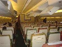 The interior of a DC-10 aircraft showing the backs of seats. The overhead lockers are mostly open.