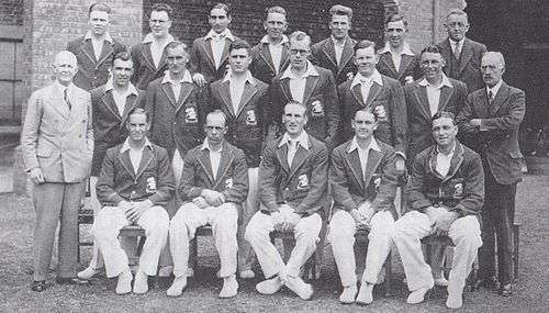 A cricket team arranged in three rows. Seventeen men are dressed as players, the other three men are in suits.