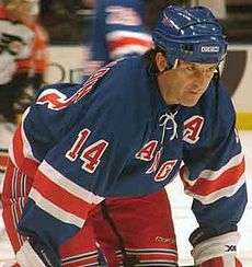 Hockey player in blue uniform. He crouches, looking downward.