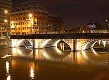 A three-arched bridge viewed from an oblique angle, illuminated by lights