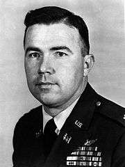  A black and white image of Bruce Crandall in his military dress uniform. He is facing the camera and turned slightly to the left