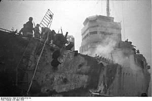 large holes in side of the ship. A ladder leads to the dock. There is also evidence of a fire.