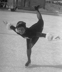 A woman wearing a dress and gloves is skating on an ice rink